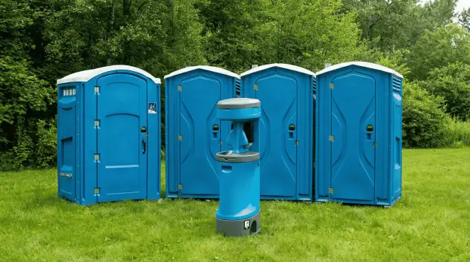 Four blue portable toilets and a matching hand washing station on grass near trees, a common sight at local outdoor events in Jersey City, NJ