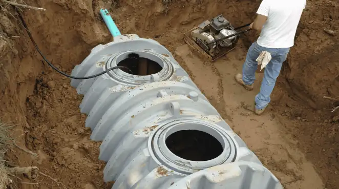 Septic tank installation showing a technician compacting soil around a new poly septic tank in an excavation pit in Jersey City, NJ